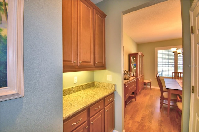 kitchen with light wood-type flooring, an inviting chandelier, and light stone counters