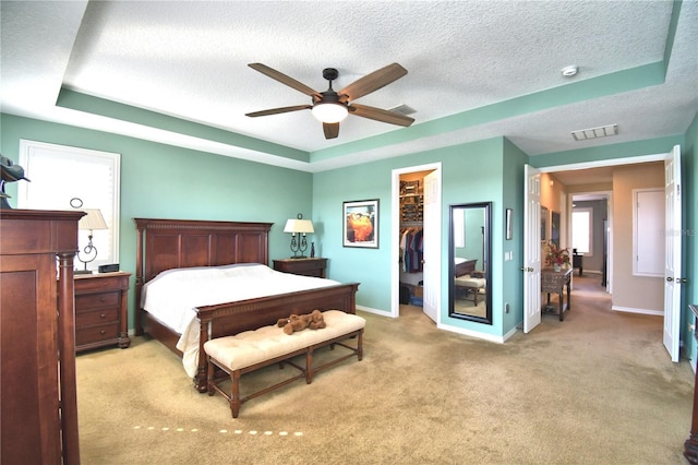 carpeted bedroom featuring a closet, a tray ceiling, a textured ceiling, and a spacious closet