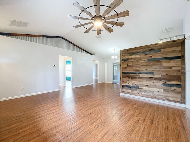 unfurnished living room with hardwood / wood-style floors, ceiling fan with notable chandelier, wooden walls, and vaulted ceiling