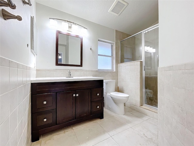 bathroom featuring toilet, a textured ceiling, tile walls, vanity, and a shower with door