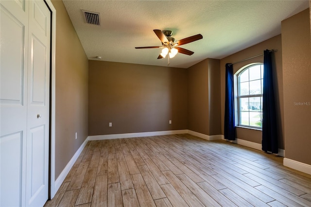 spare room featuring a textured ceiling, visible vents, light wood-style flooring, and ceiling fan