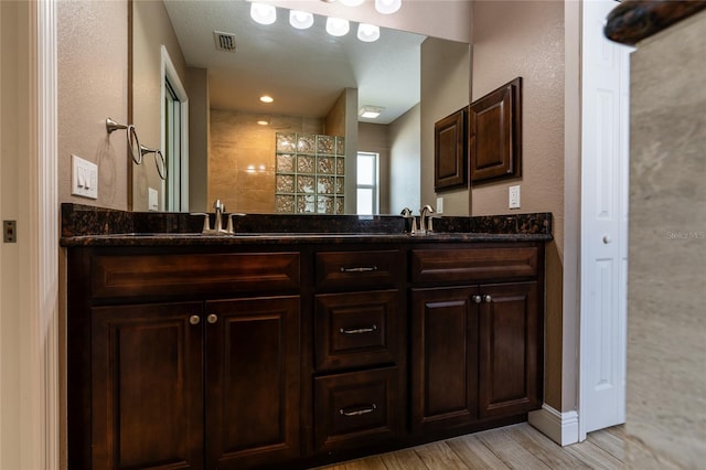 bathroom with double vanity, visible vents, wood finished floors, and a walk in shower