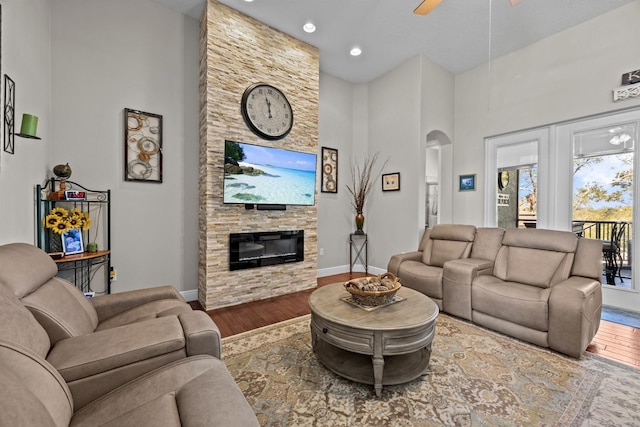 living room featuring hardwood / wood-style floors, a fireplace, ceiling fan, and a high ceiling