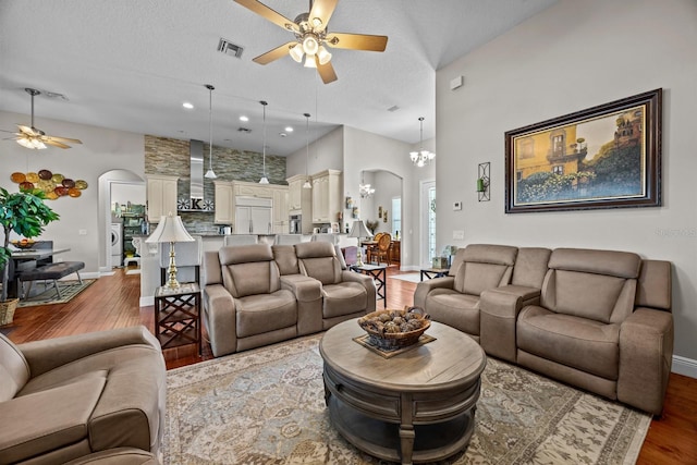 living room featuring a towering ceiling, wood-type flooring, ceiling fan with notable chandelier, and a textured ceiling