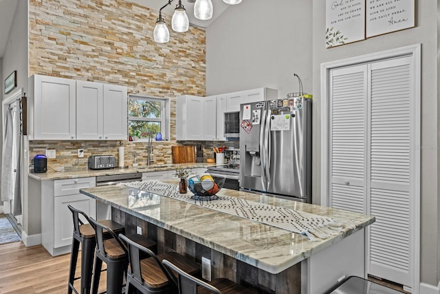 kitchen featuring a breakfast bar, pendant lighting, a center island, stainless steel appliances, and light stone countertops