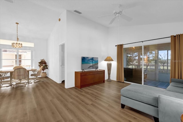 living room with ceiling fan with notable chandelier, wood-type flooring, and high vaulted ceiling