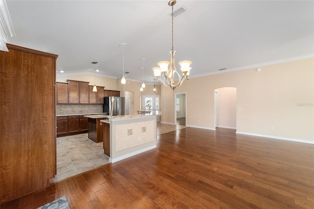 kitchen featuring a kitchen island with sink, decorative backsplash, stainless steel refrigerator, and decorative light fixtures