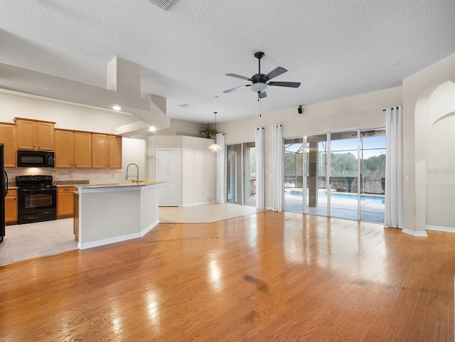 kitchen featuring tasteful backsplash, a center island with sink, ceiling fan, light hardwood / wood-style floors, and black appliances