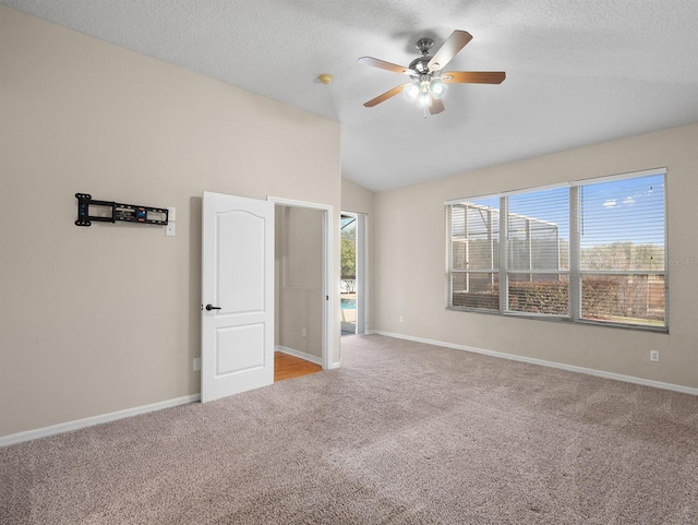 empty room with vaulted ceiling, light carpet, ceiling fan, and a textured ceiling