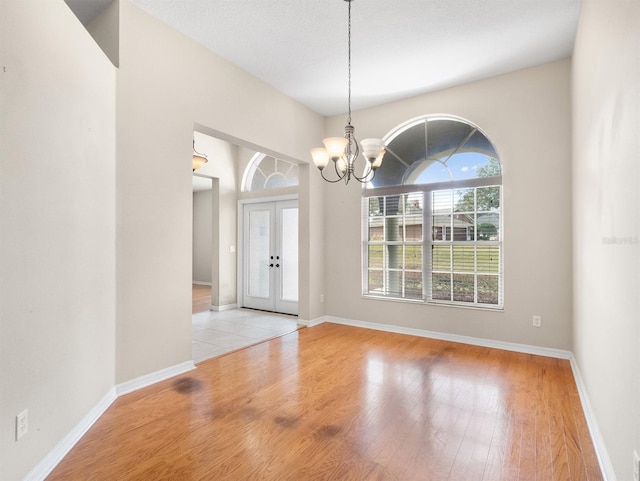 unfurnished dining area featuring french doors, light hardwood / wood-style flooring, and a notable chandelier