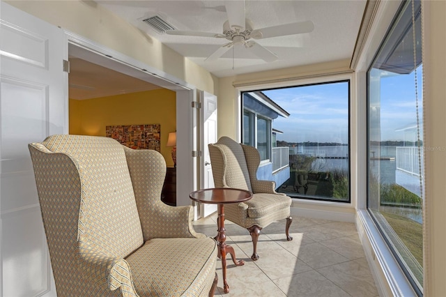 living area with light tile patterned floors, ceiling fan, and a water view