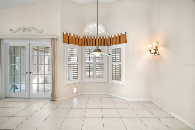 unfurnished dining area featuring french doors, a towering ceiling, and light tile patterned floors