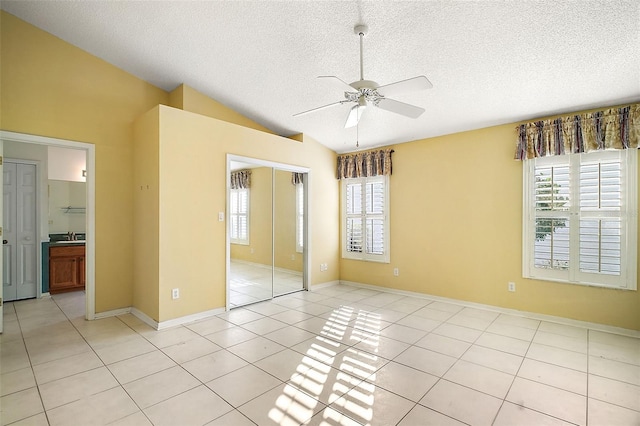 unfurnished bedroom featuring light tile patterned flooring, vaulted ceiling, a textured ceiling, and a closet