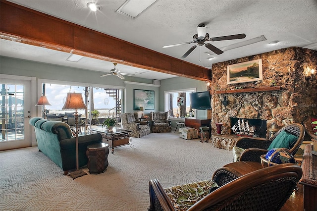 carpeted living room featuring beam ceiling, ceiling fan, a stone fireplace, and a textured ceiling