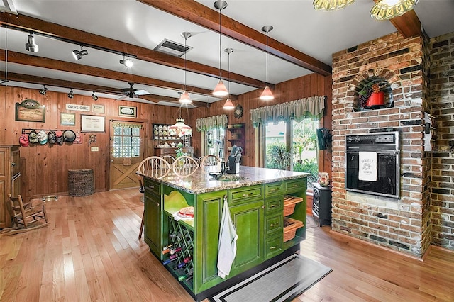kitchen featuring green cabinetry, an island with sink, pendant lighting, light stone countertops, and light hardwood / wood-style floors