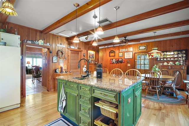 kitchen with sink, green cabinets, white refrigerator, light stone countertops, and a center island with sink
