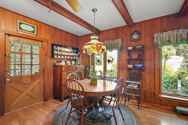 dining space with light hardwood / wood-style flooring, wooden walls, and beamed ceiling