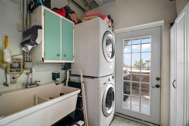 laundry area with stacked washer / dryer, sink, and cabinets
