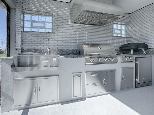 interior space with stone countertops, refrigerator, wall chimney range hood, and brick wall