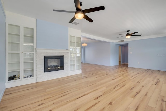 unfurnished living room featuring a fireplace, built in features, ceiling fan, and light wood-type flooring