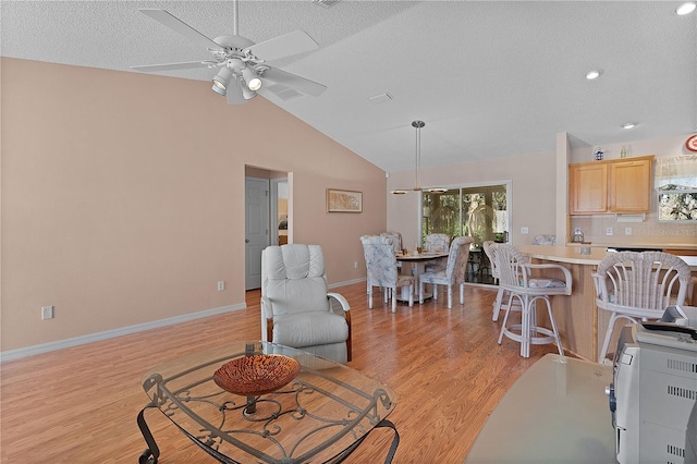 living room with a textured ceiling, vaulted ceiling, ceiling fan, and light wood-type flooring