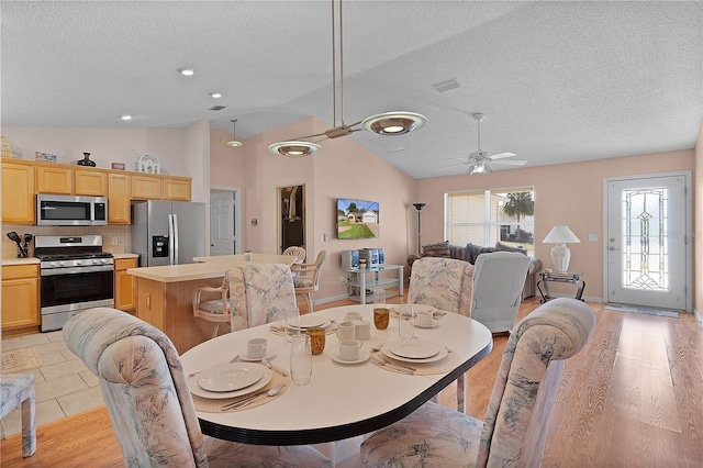 dining space with ceiling fan, vaulted ceiling, a textured ceiling, and light wood-type flooring