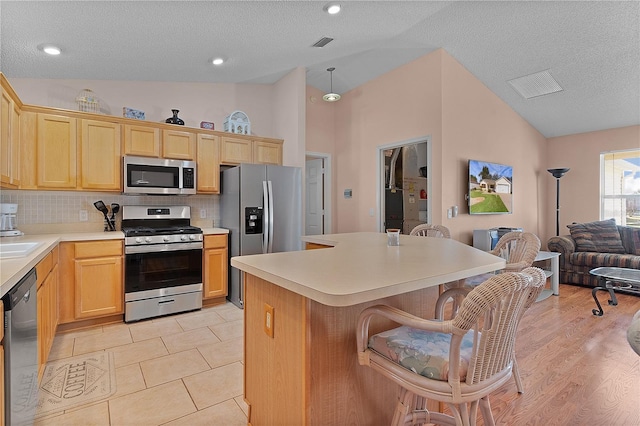 kitchen featuring lofted ceiling, a center island, light brown cabinets, appliances with stainless steel finishes, and backsplash