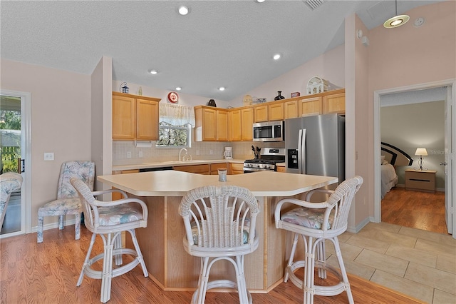 kitchen featuring appliances with stainless steel finishes, a center island, light brown cabinets, and a kitchen bar