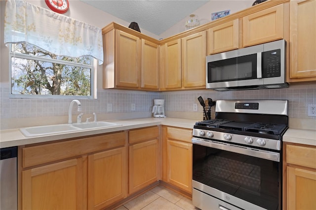 kitchen featuring appliances with stainless steel finishes, lofted ceiling, sink, light tile patterned floors, and a textured ceiling