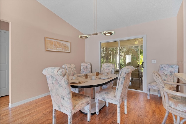 dining room featuring lofted ceiling, a textured ceiling, and light wood-type flooring