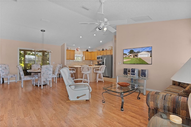 living room with light hardwood / wood-style flooring, ceiling fan, vaulted ceiling, and a textured ceiling