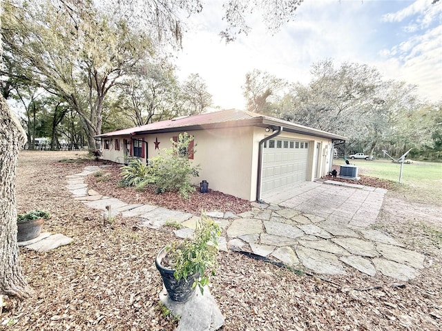 view of home's exterior with an attached garage, driveway, cooling unit, and stucco siding