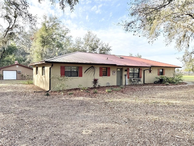 single story home with an outbuilding, a detached garage, stucco siding, metal roof, and driveway