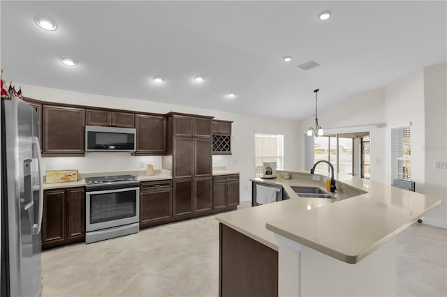 kitchen featuring pendant lighting, lofted ceiling, sink, stainless steel appliances, and a center island with sink