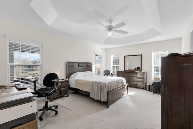 bedroom with multiple windows, a tray ceiling, light carpet, and ceiling fan