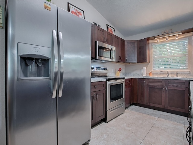 kitchen with lofted ceiling, sink, light stone counters, stainless steel appliances, and dark brown cabinets