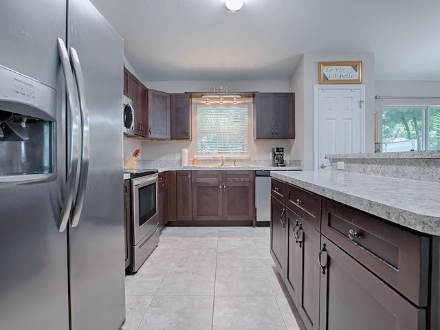 kitchen featuring a healthy amount of sunlight, dark brown cabinetry, appliances with stainless steel finishes, and light tile patterned floors