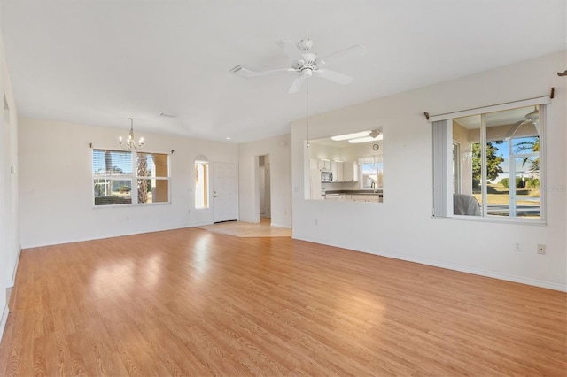 unfurnished living room featuring plenty of natural light, ceiling fan with notable chandelier, and light hardwood / wood-style floors