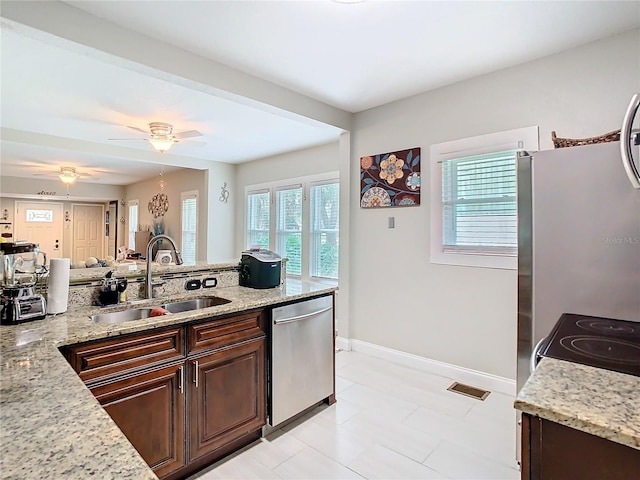 kitchen featuring light stone counters, dark brown cabinetry, dishwasher, and sink