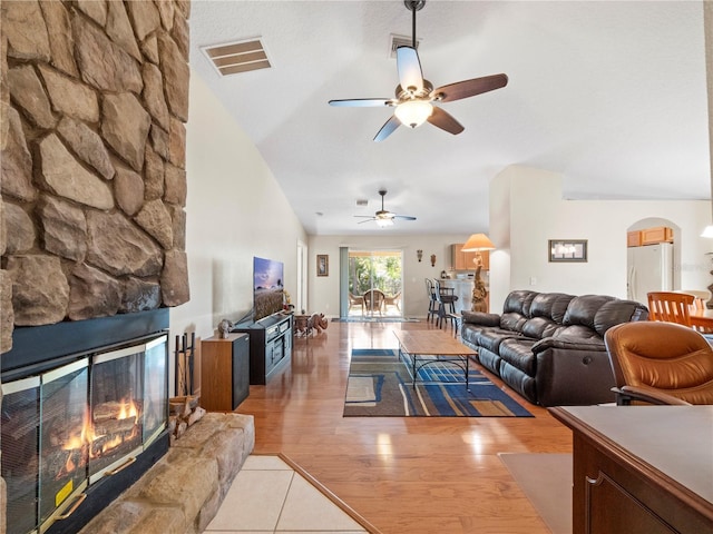 living room with vaulted ceiling, ceiling fan, a stone fireplace, and light wood-type flooring