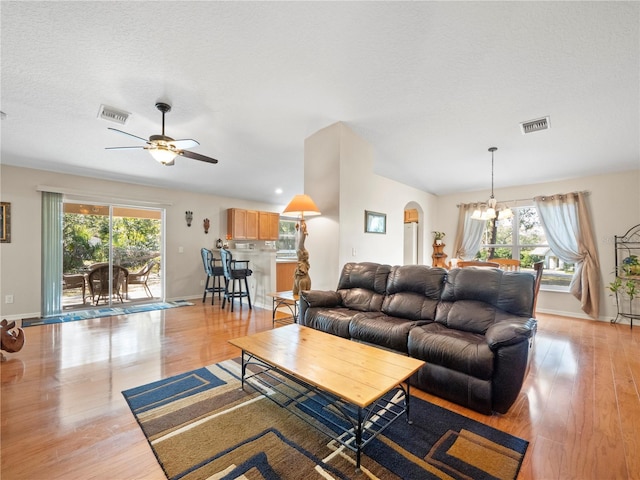 living room featuring ceiling fan with notable chandelier, a textured ceiling, and light wood-type flooring