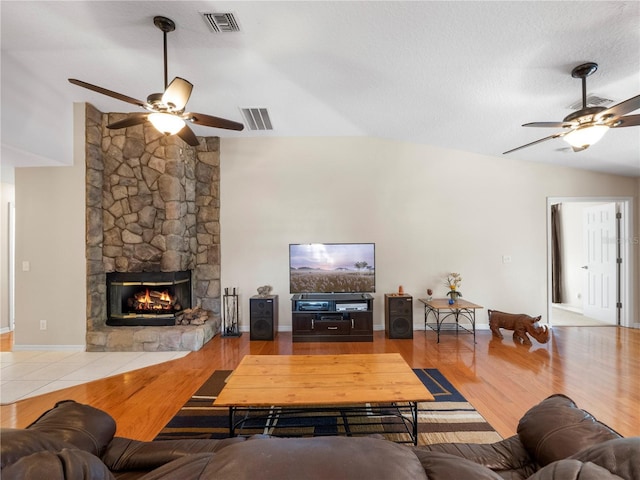 living room featuring ceiling fan, lofted ceiling, a fireplace, and light hardwood / wood-style floors