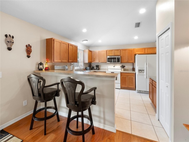 kitchen featuring a breakfast bar, sink, kitchen peninsula, white appliances, and light hardwood / wood-style floors