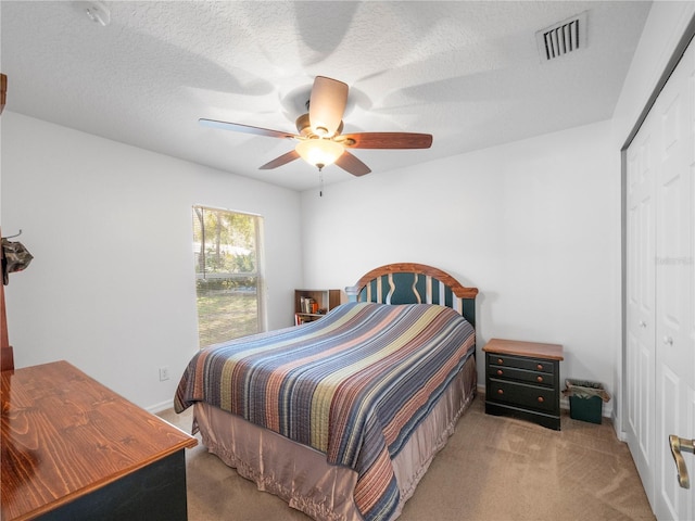 bedroom with ceiling fan, light carpet, a textured ceiling, and a closet