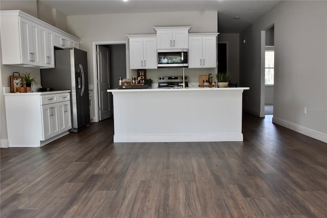 kitchen featuring stainless steel appliances, white cabinetry, dark wood-type flooring, and a kitchen island with sink