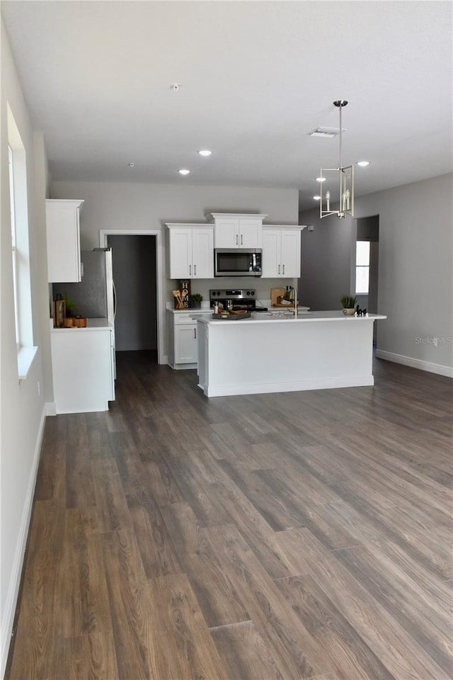 kitchen with dark wood-type flooring, white cabinetry, hanging light fixtures, stainless steel appliances, and a kitchen island with sink