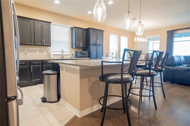 kitchen with stainless steel fridge, a kitchen breakfast bar, hanging light fixtures, a center island, and light stone countertops