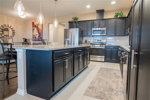 kitchen featuring a kitchen bar, light stone counters, an island with sink, stainless steel appliances, and decorative backsplash