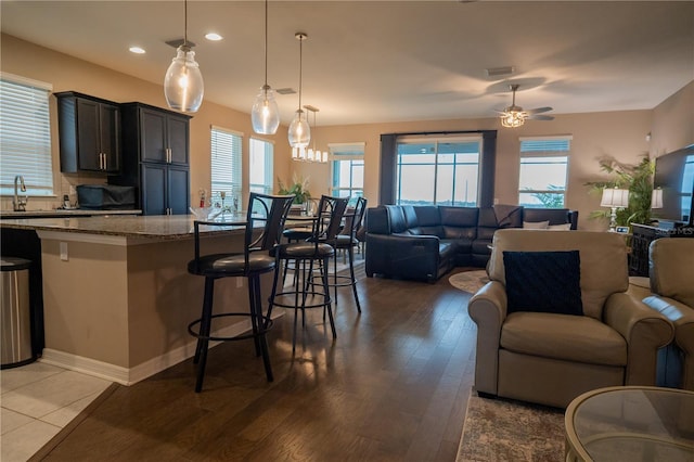 kitchen with light stone counters, a kitchen bar, hanging light fixtures, and a wealth of natural light