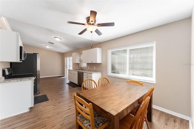 dining space featuring lofted ceiling, sink, light wood-type flooring, ceiling fan, and a textured ceiling